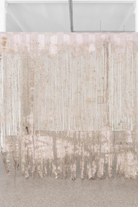 Grande pièce de tissu translucide suspendue, aux teintes pâles et abîmée en bas, avec des motifs verticaux blancs, dans une galerie blanche minimaliste