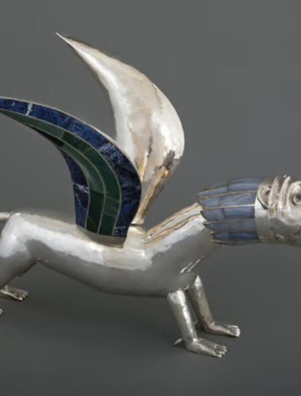Sculpture en métal poli représentant une créature mythologique hybride, dotée d’un corps de lion et d’ailes incrustées de motifs colorés. L’œuvre se distingue par ses lignes stylisées et son expression saisissante.
