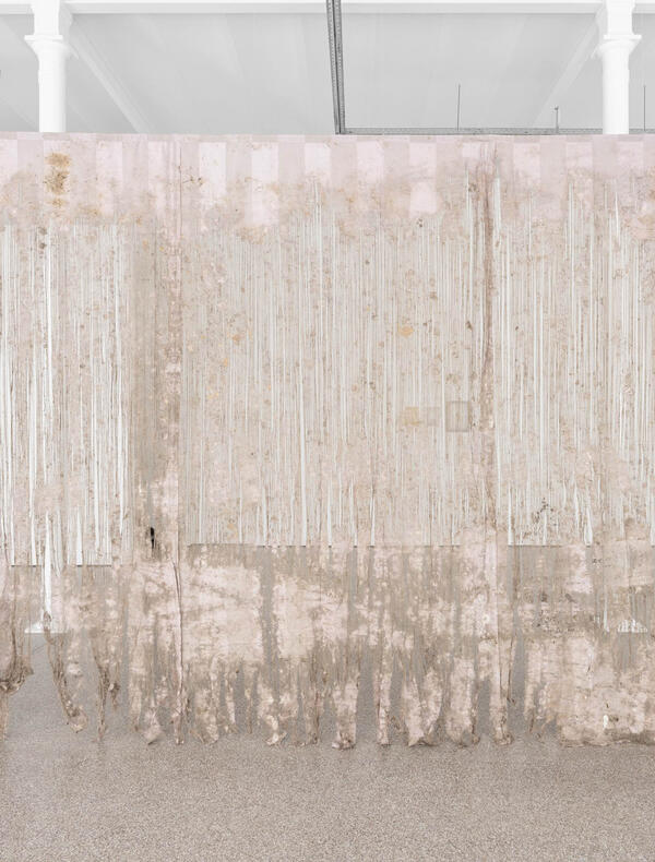 Grande pièce de tissu translucide suspendue, aux teintes pâles et abîmée en bas, avec des motifs verticaux blancs, dans une galerie blanche minimaliste