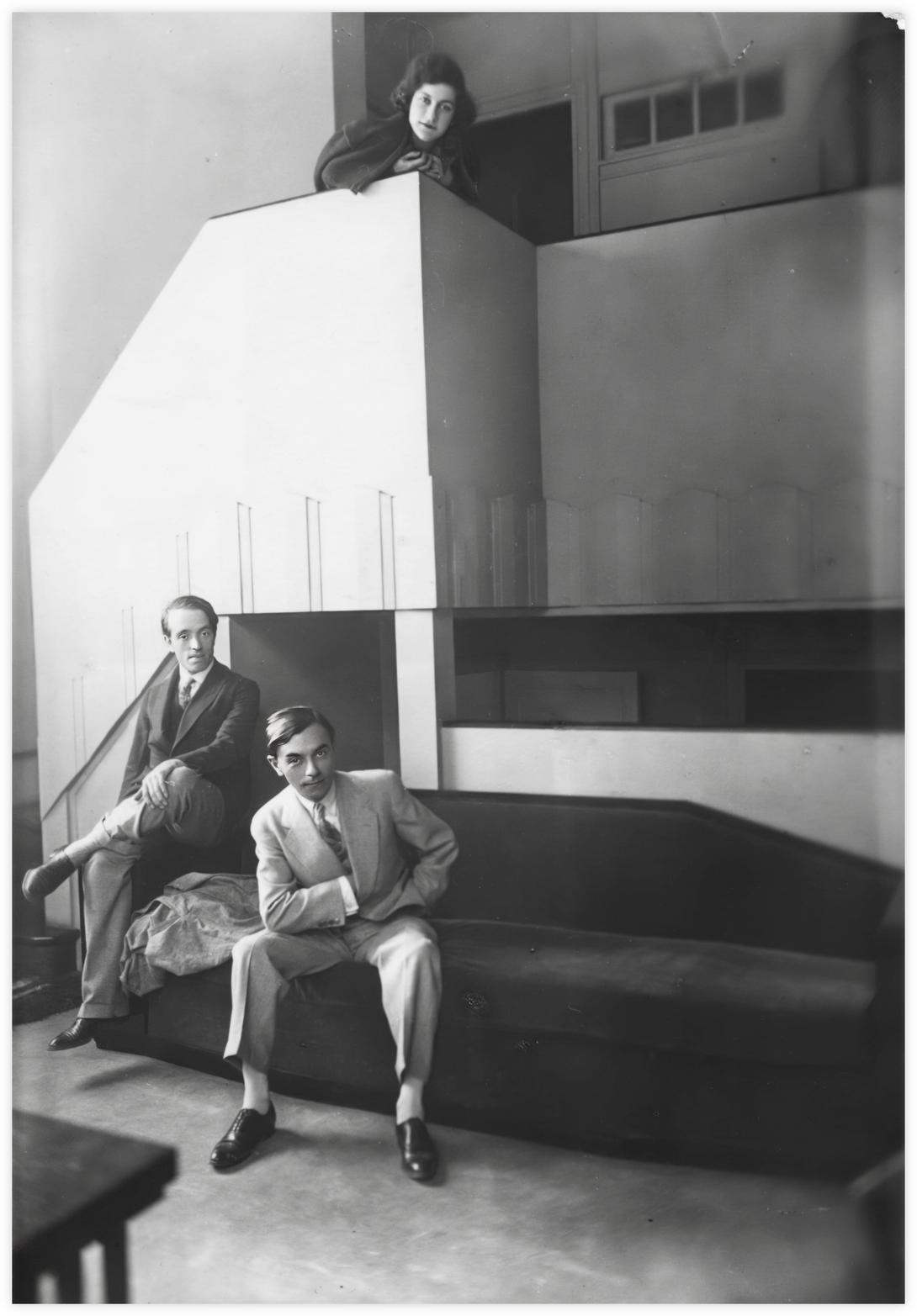 32 Daria, Imre et Lahner, Paris, photo Alban Imre Gyomaï est assis sur la banquette, la main à l'intérieur de sa veste, Emile Lahner est assis sur l'accoudoir du canapé, les jambes croisées. Daria est montée en haut de l'escalier et se penche pardessus le bord, tous les trois regardent le photographe. Photo Alban, Paris autour de 1930.